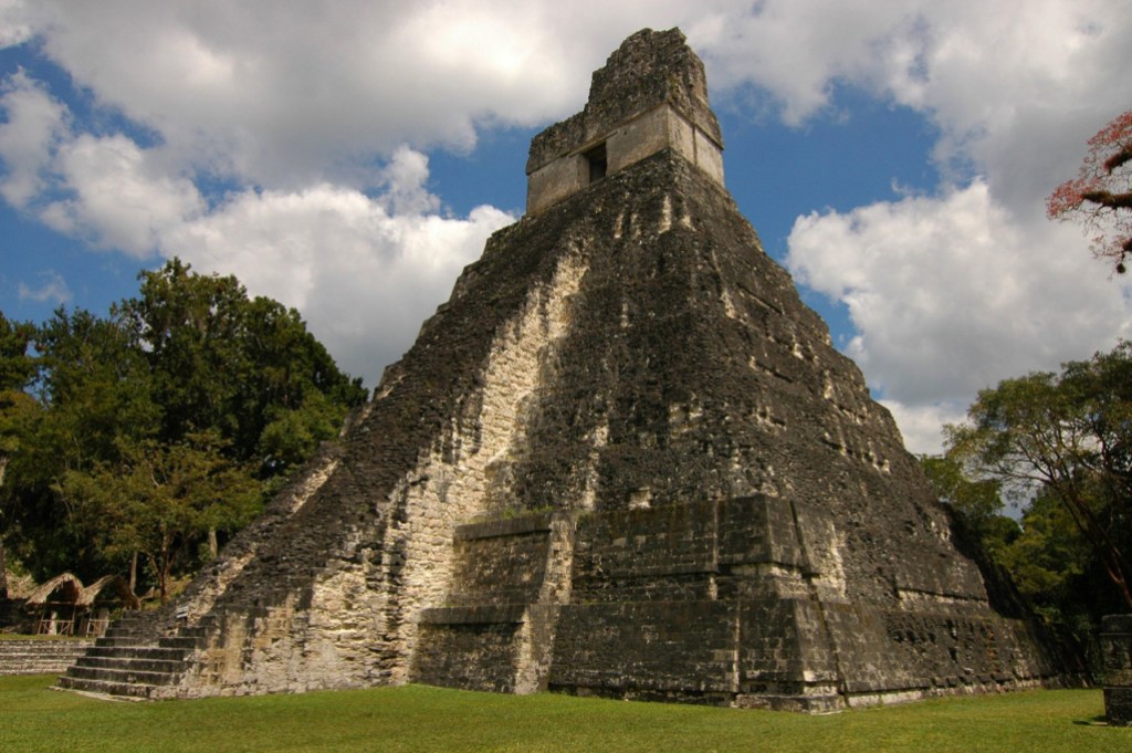 Photo of a pyramidal Maya temple at Tikal with pale stones showing through moss.