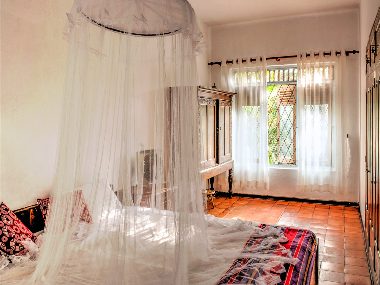 A mosquito net hanging above a bed in a colonial style bedroom with tile floor.