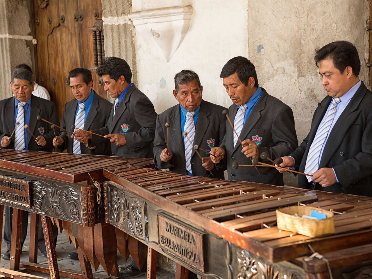 A row of musicians in suit and tie play marimba in front of a colonial style building in Antigua, Guatemala.