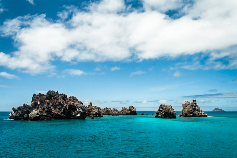 Low, pointy rock formations stick out of turquoise sea under blue cloudy sky.