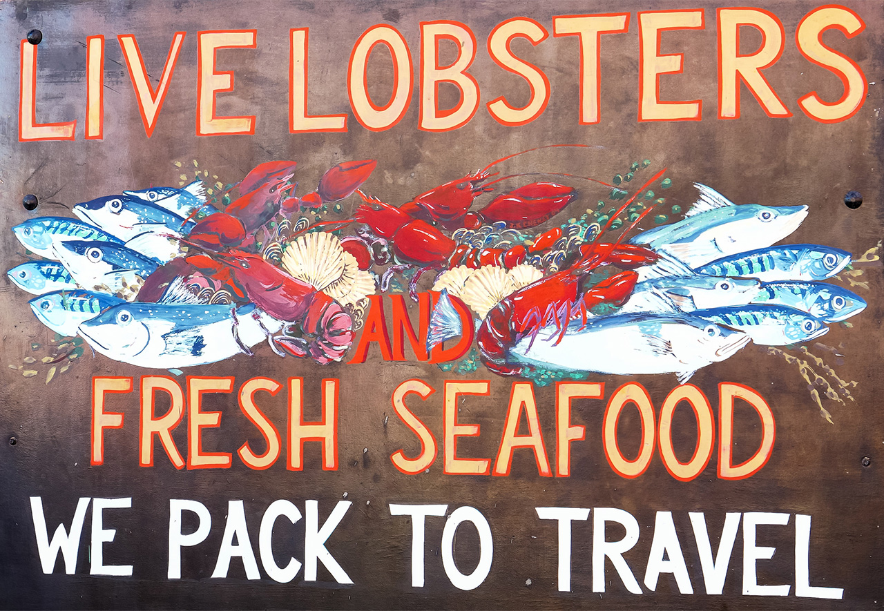 A handpainted sign advertising live lobsters and fresh seafood for sale.