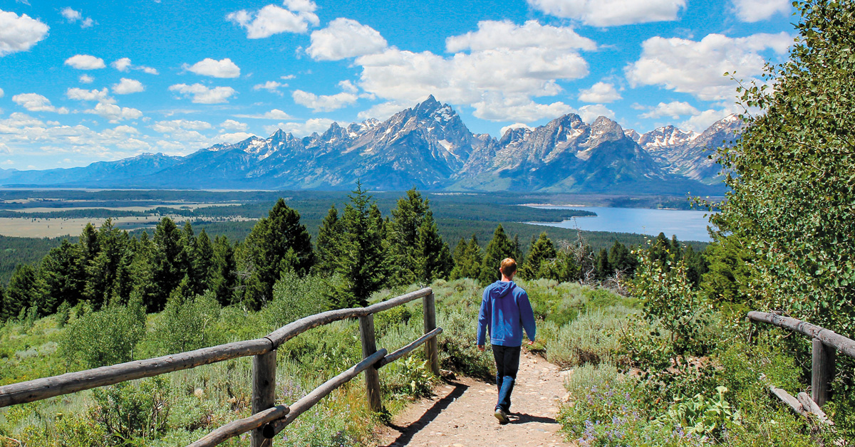 person in blue hoodie walking on a nature trail with mountains in the distance