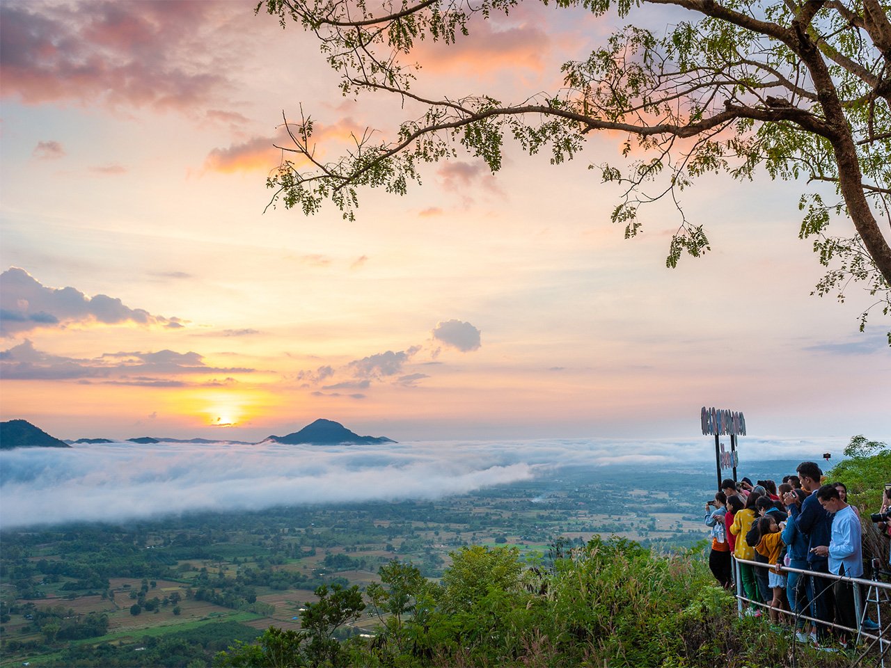 A viewpoint overlooks a dramatic sunset as fog rolls into a valley in Loei Province, Thailand.