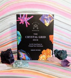 Photo of "Mystic Mondays: The Crystal Grid Deck" surrounded by various crystals against a colorful marbled background