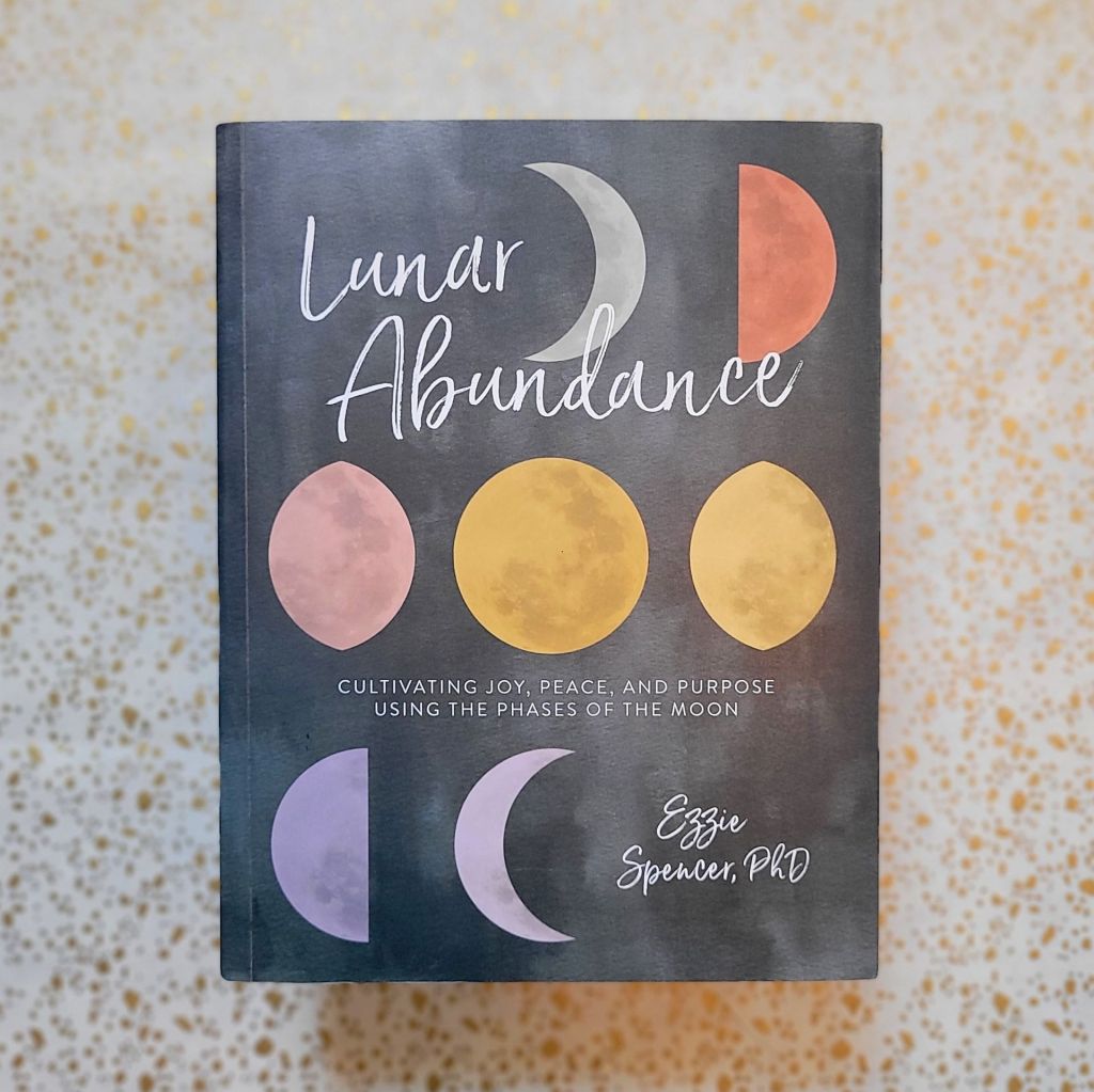 Photo of “Lunar Abundance: Cultivating Joy, Peace, and Purpose Using the Phases of the Moon” laid above a gold and white backdrop