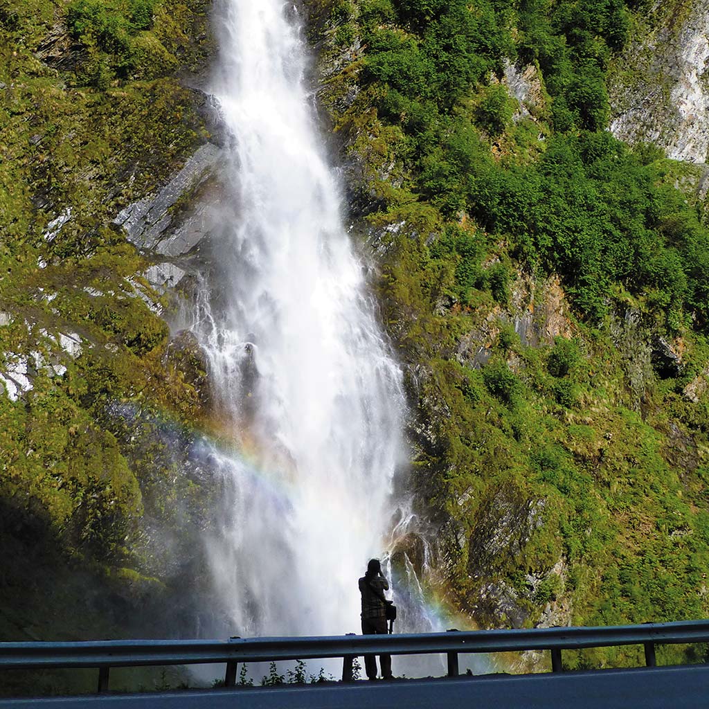 A woman stands and admires the cascading Bridal Falls from a lookout point