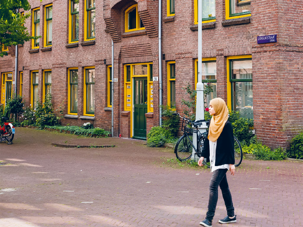 girl walking on the sidewalk beside the brick buildings of berlageblokken in Amsterdam