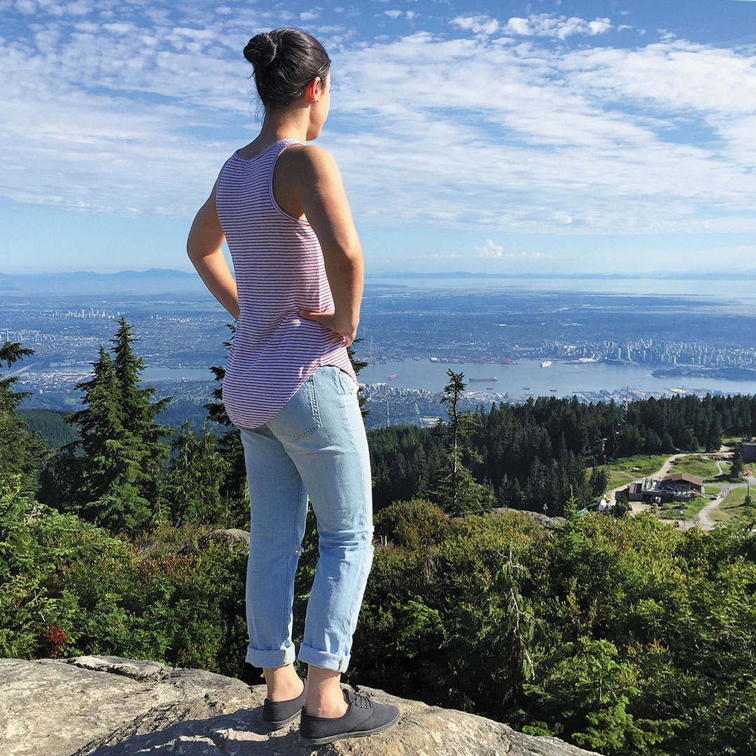 a woman stands atop Grouse Mountain looking out at Vancouver