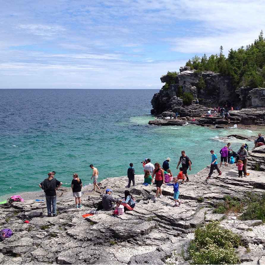 People stand at the edge of a rocky bank, overlooking blue water at Bruce Peninsula National Park