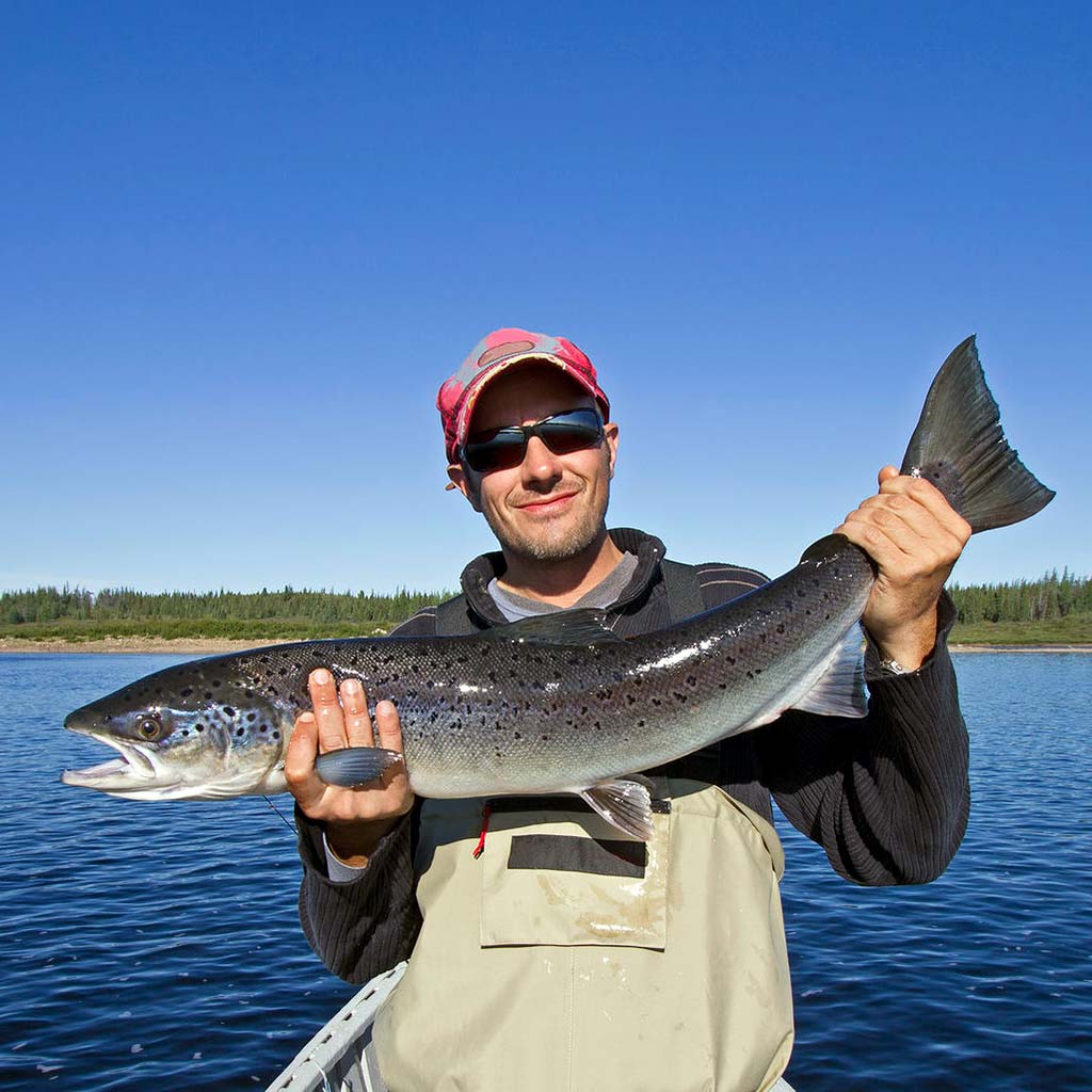A fisherman proudly carries a freshly-caught Atlantic Salmon.