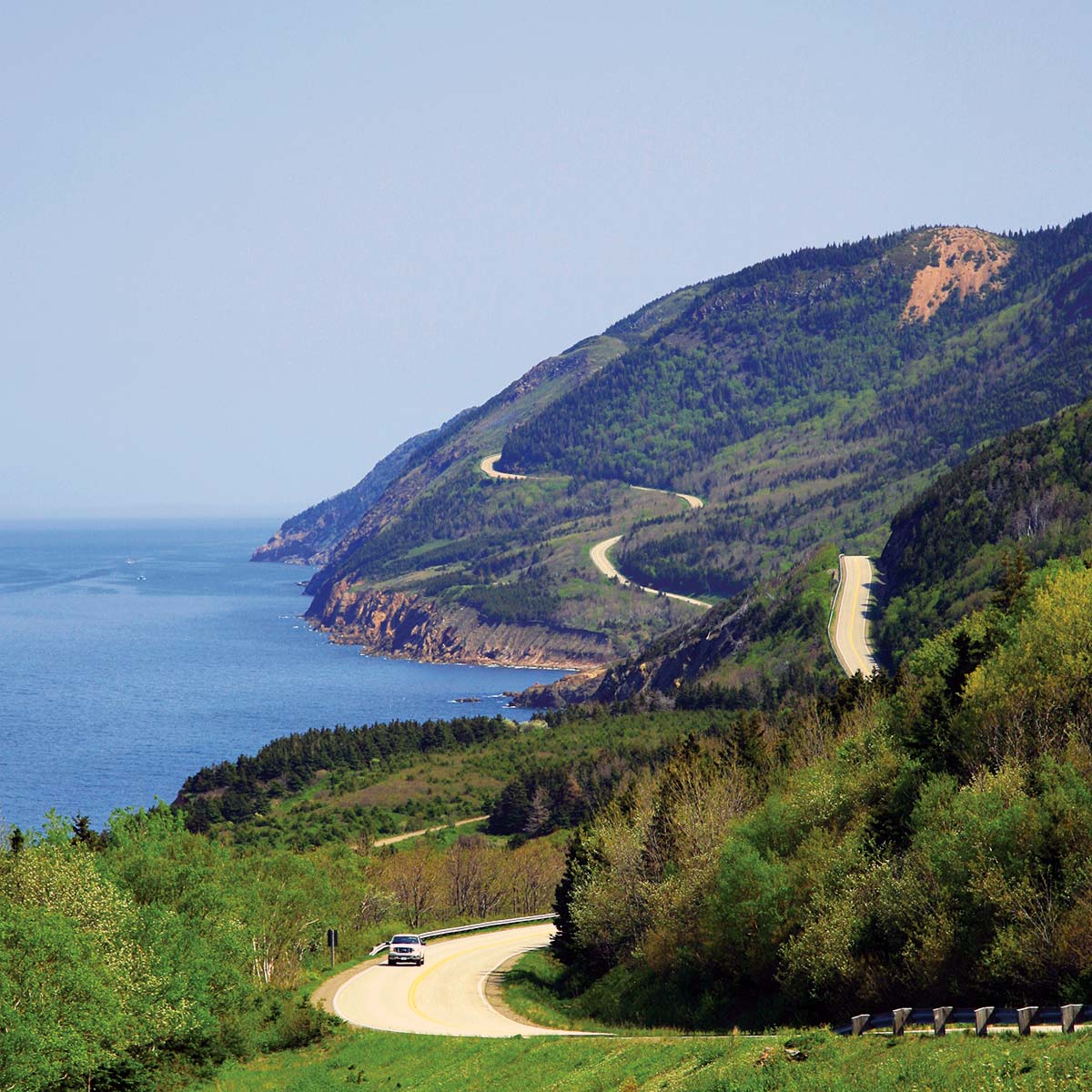 A car traverses the windy coastal Cabot Trail highway in Cape Breton Highlands National Park.
