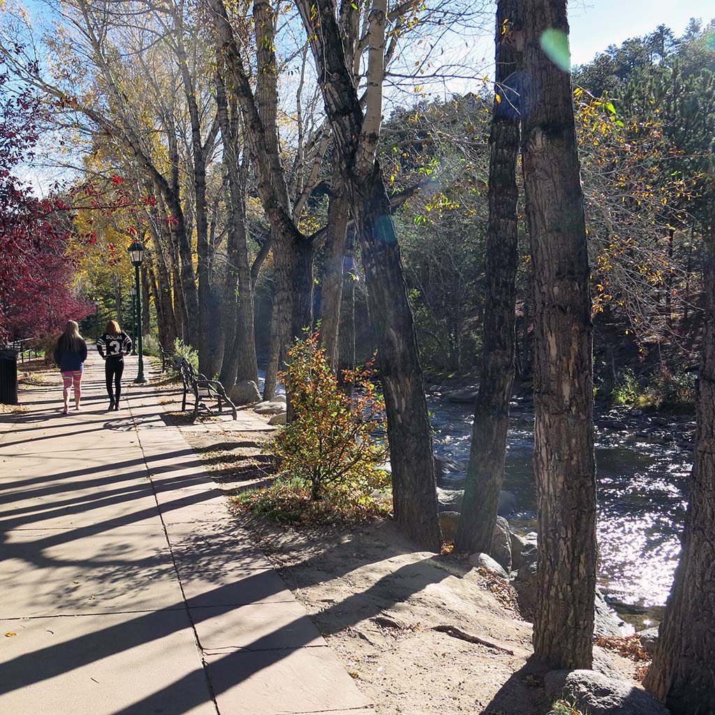 Pedestrians on a tree-lined paved path alongside the Fall River.
