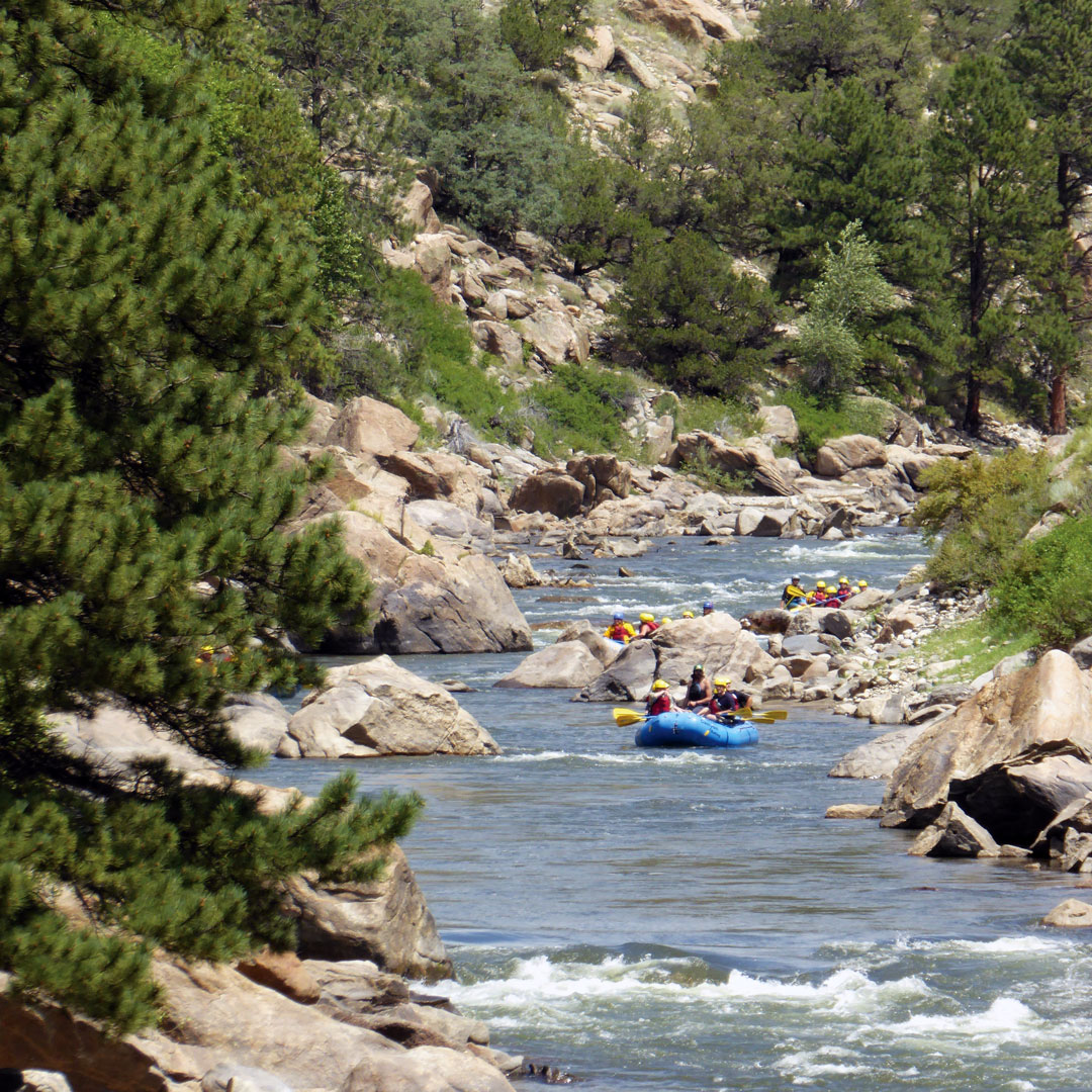 rafts full of people on the Roaring Fork river surrounded by rocks and trees