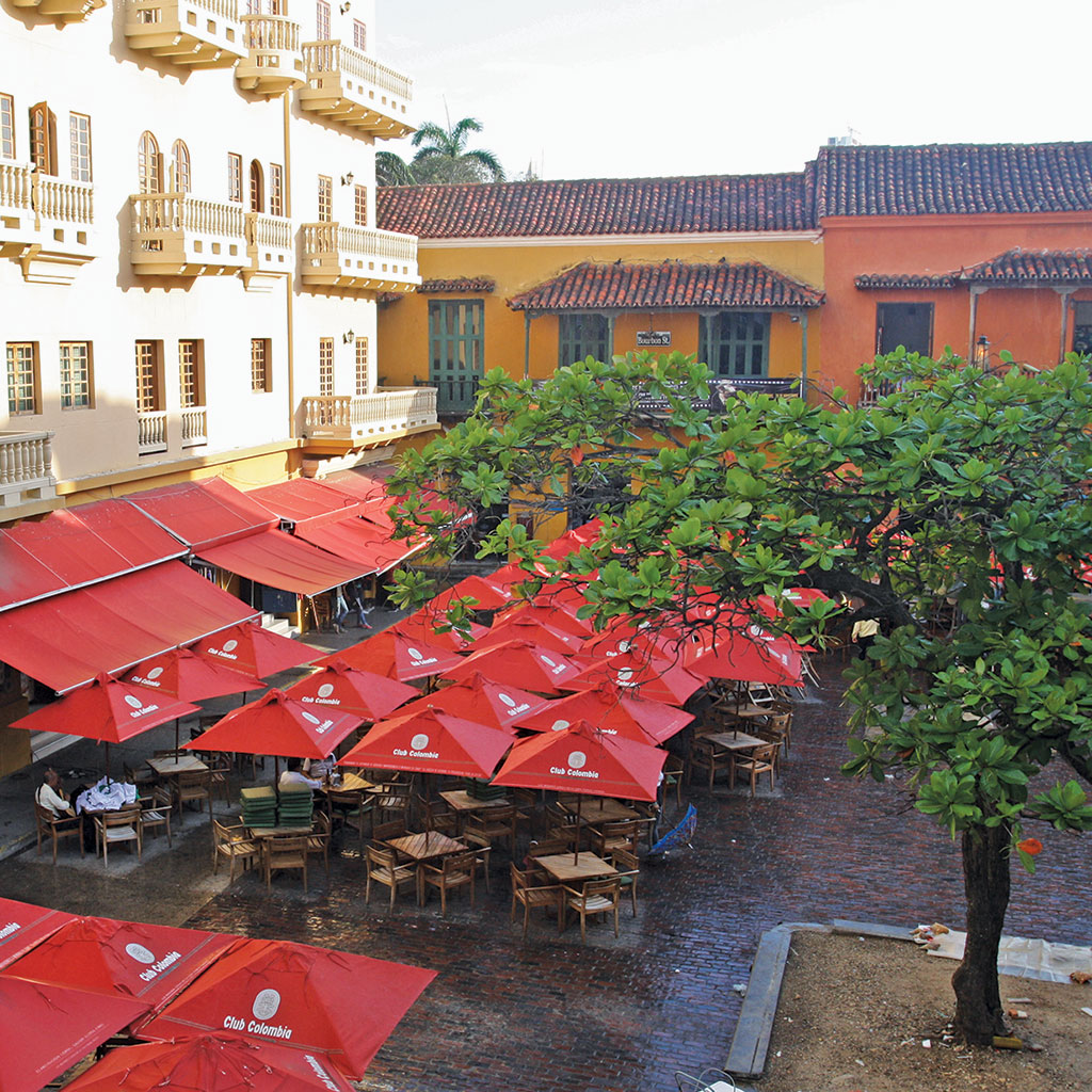 Red umbrellas shade seating in Cartagena's Plaza de Santo Domingo.