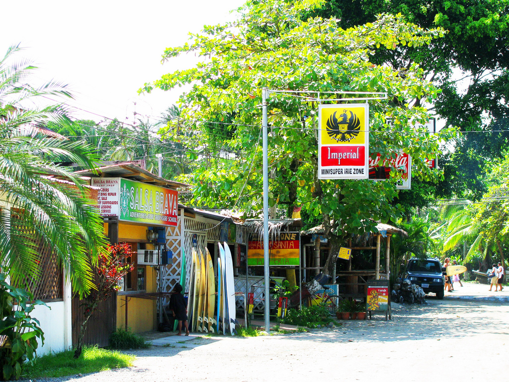 Surfboards are lined up in front of a surfshop painted in rastafarian colors.