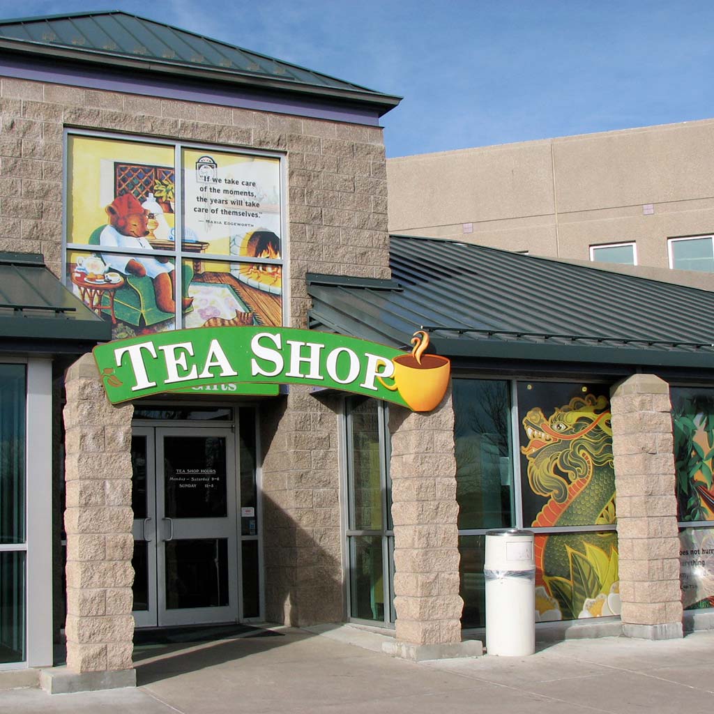 Storefront with a logo and overhanging green sign that reads TEA SHOP