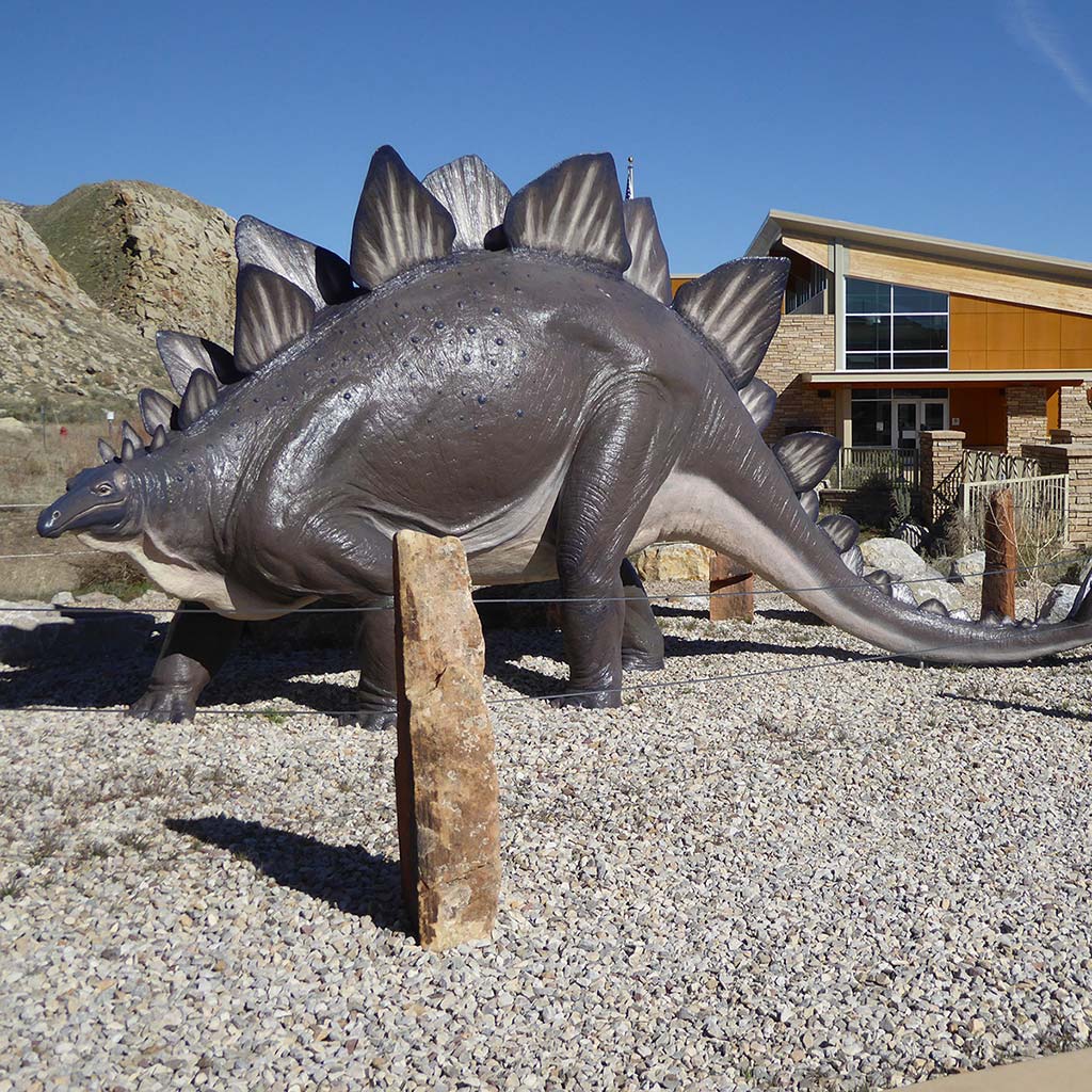 A dinosaur sculpture stands in front of the visitors center on loose gravel