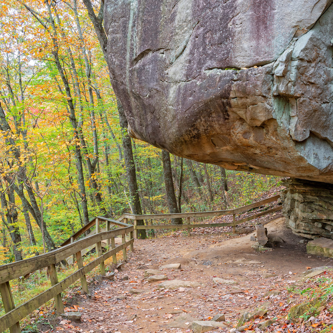 hiking trail under a large rock through trees