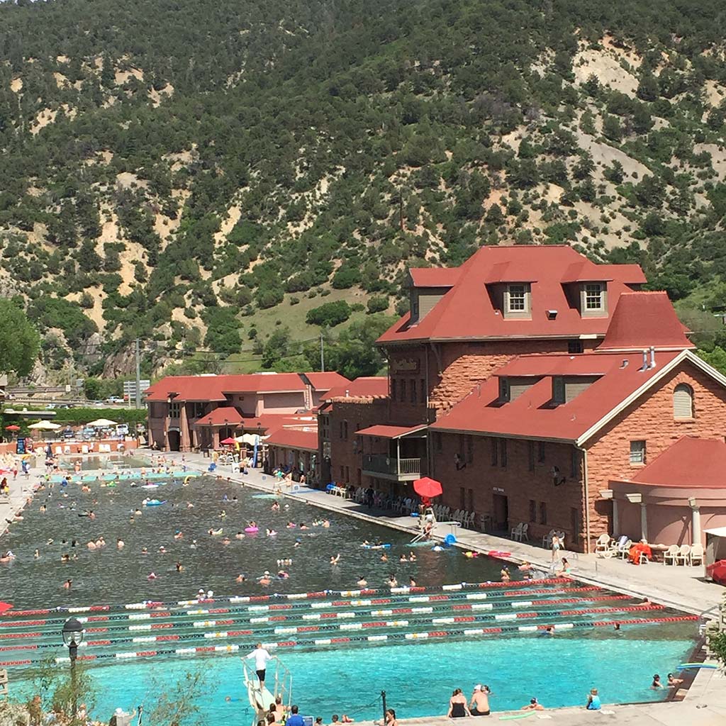 A long pool next to a red bath house with a green and dusty hill in the background