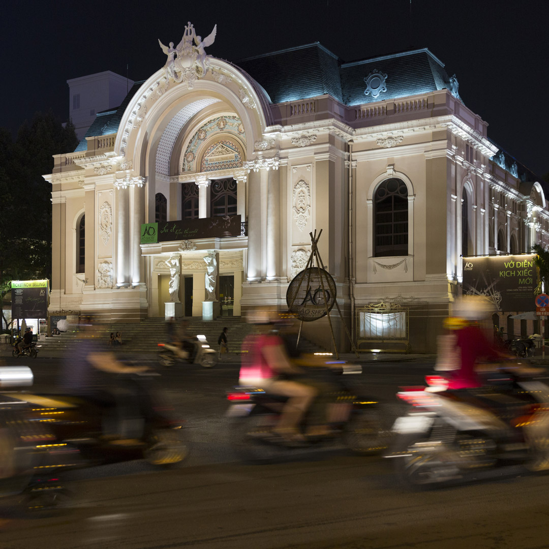 motorcyclists driving by the Ho Chi Minh City Opera House at night