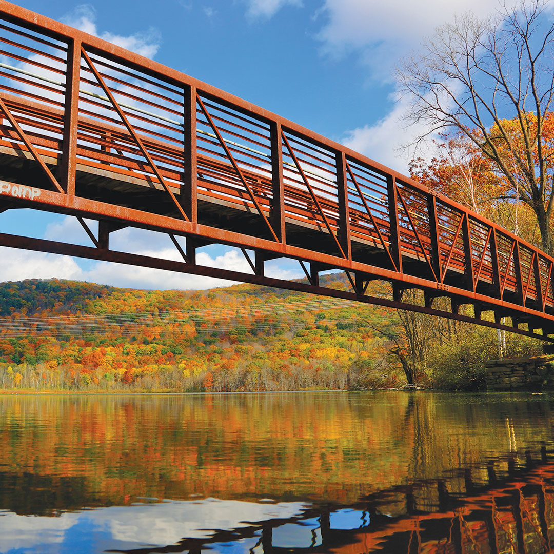 rusty bridge reflected in water backed by fall color