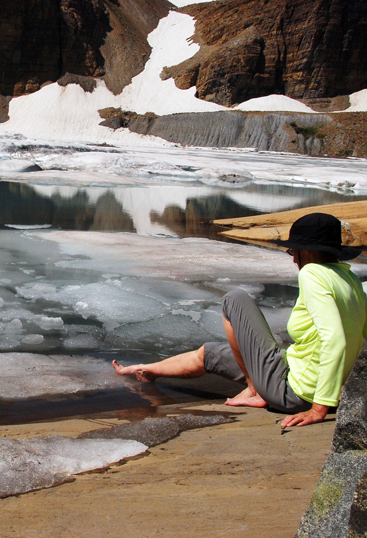 A hiker touches the glacial ice with her foot.