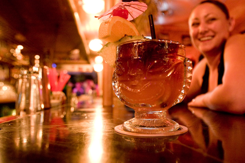 A Mai Tai on the bar with a smiling patron in the background at South Shore Tiki Lounge.