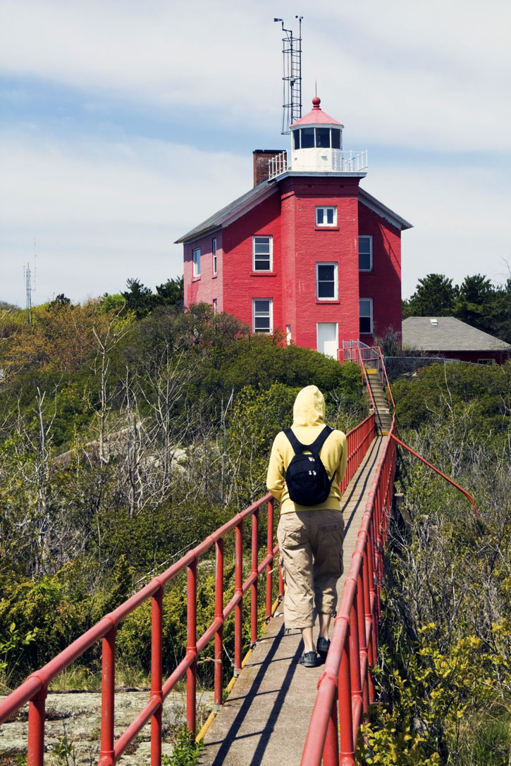 A traveler crosses a footbridge to the Marquette Harbor Lighthouse.