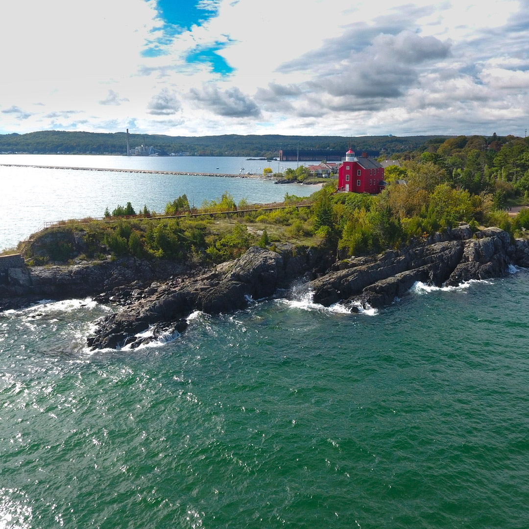 aerial view of a lighthouse on top of land jutting into lake superior