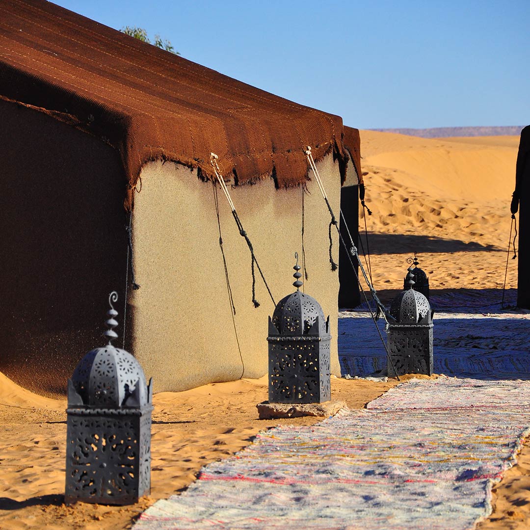 a path lined with lamps next to a desert tent in Morocco