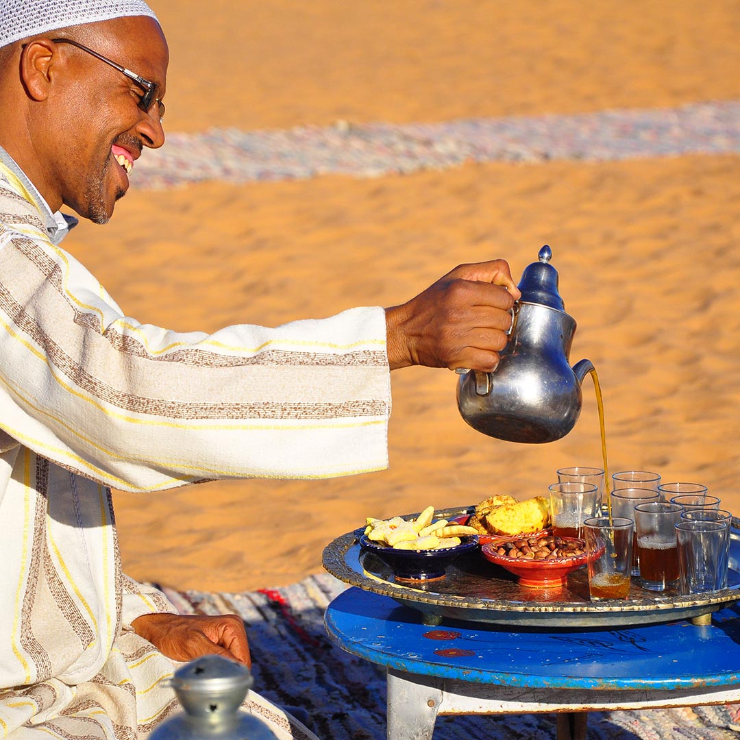 man pouring tea surrounded by Moroccan desert sand