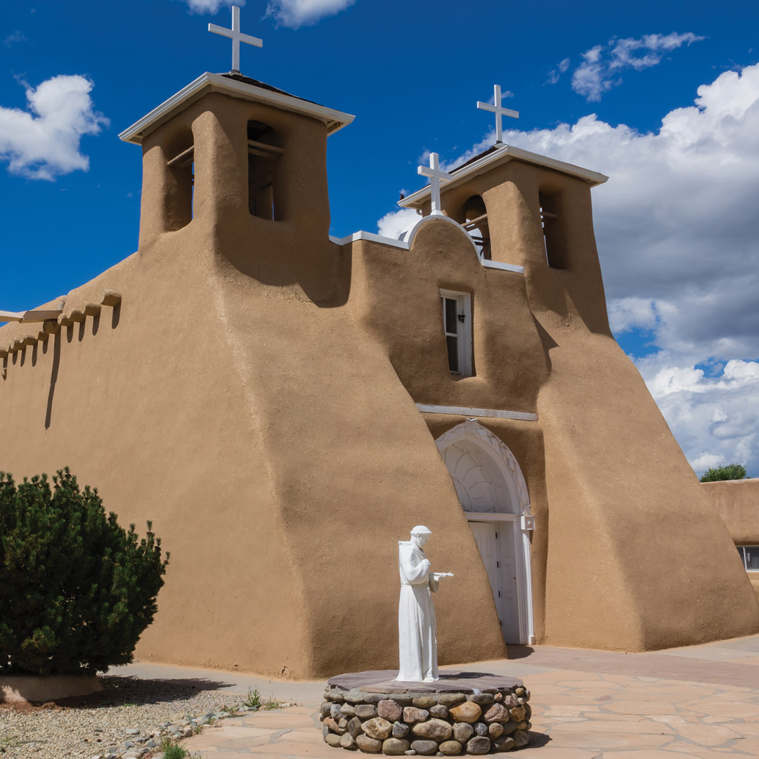 church in taos with a statue of a priest in front