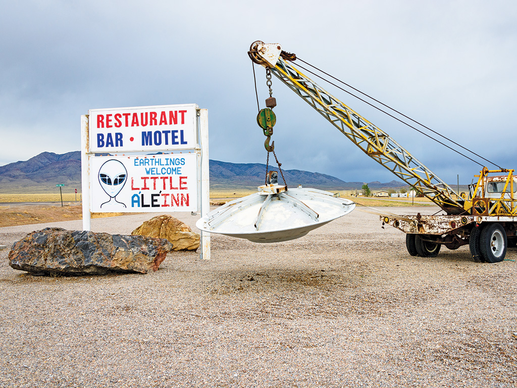 truck with a crane holding up a flying saucer sculpture next to a welcome sign in Nevada