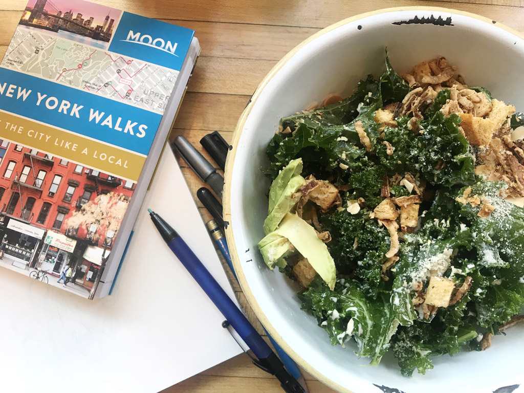 kale caesar salad next to pens and a book in New York City