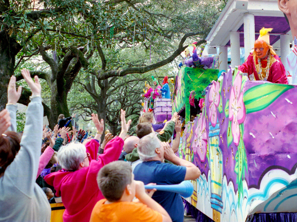 a crowd of people gathered to cheer and watch the Mardi Gras parade in New Orleans
