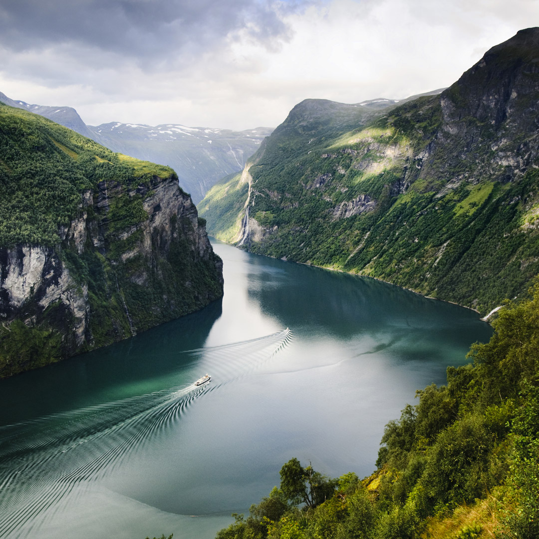 Cruise ship sails through the deep blue-green waters of Geirangerfjord