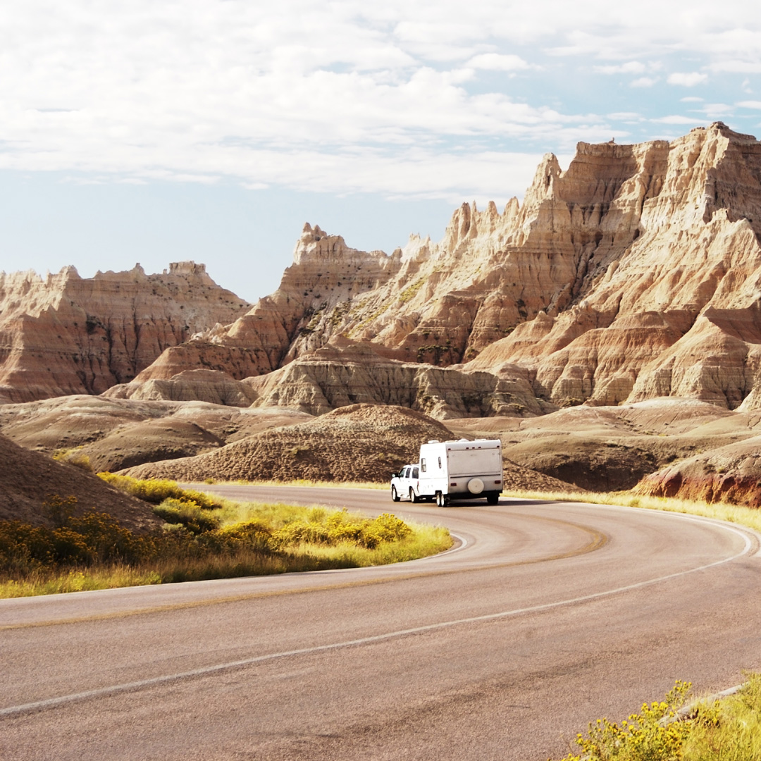 truck with camper attached driving on a winding road through Badlands National Park