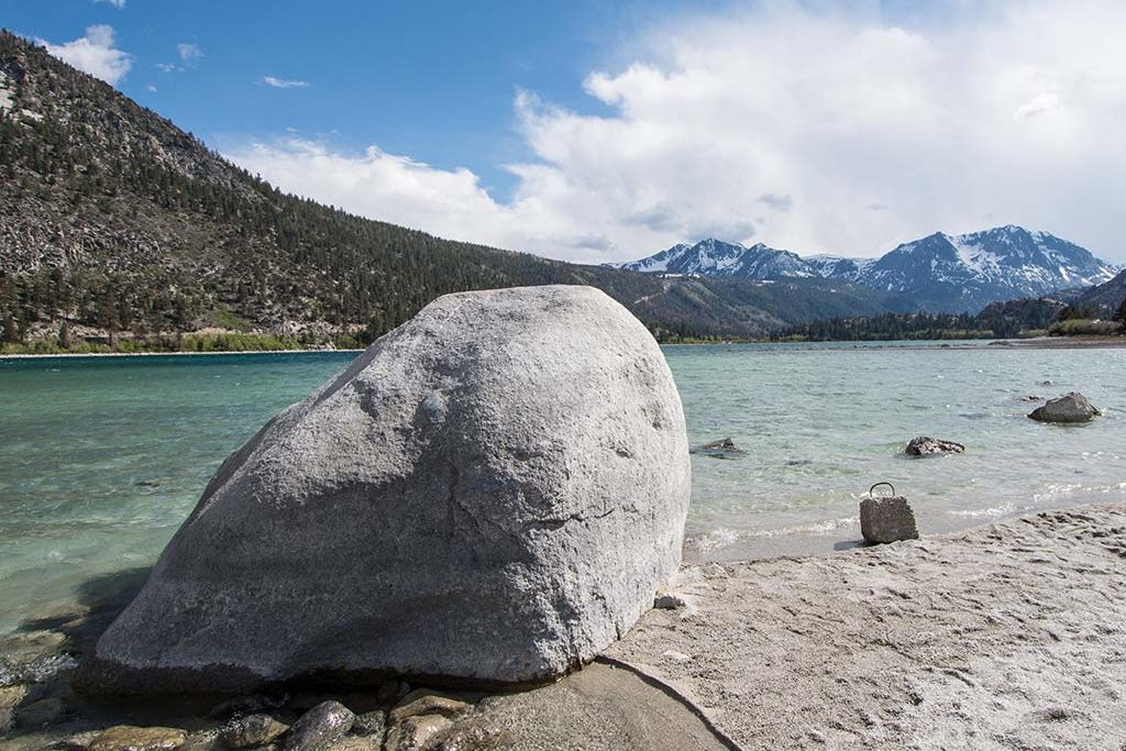 large boulder on the lakeshore of a clear aqua lake with mountains in the distance