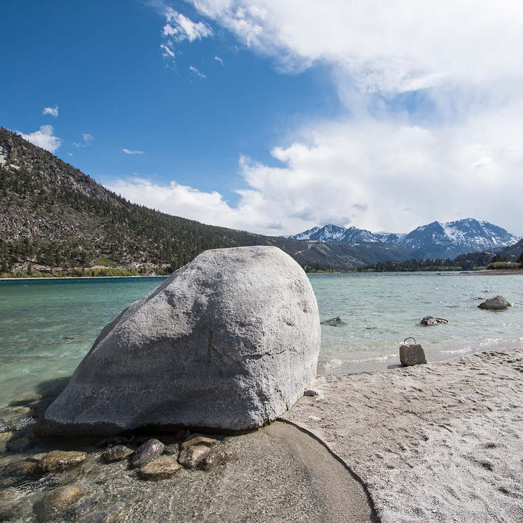 large boulder on the lakeshore of a clear aqua lake with mountains in the distance