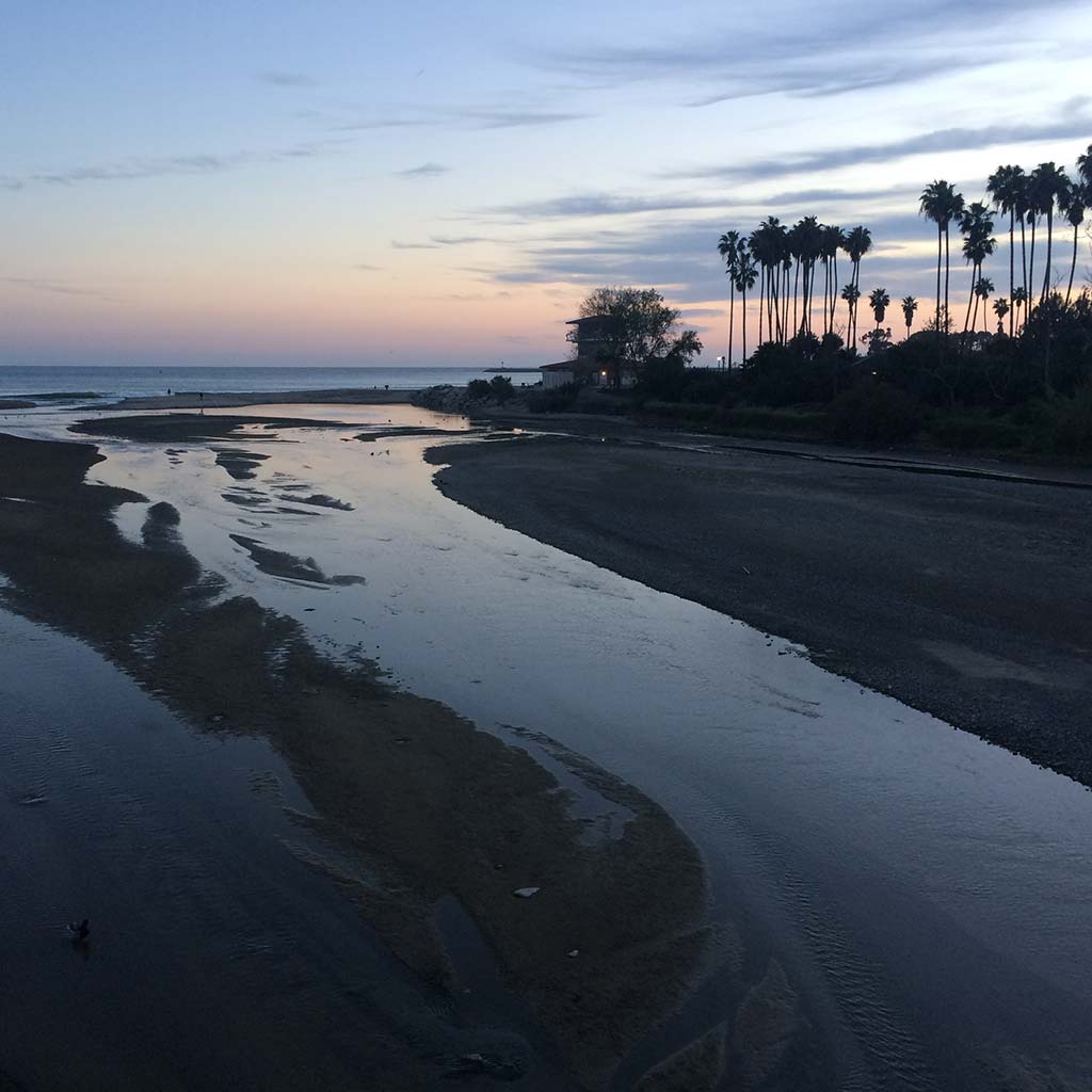 Doheny State Beach at sunset. Shallow waters come onto the sand and palm trees are visible in the distance