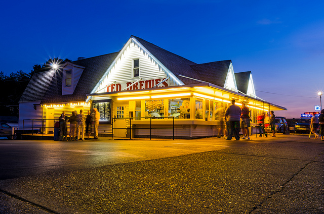 Photo of people approaching a brightly-lit Ted Drewes in evening.