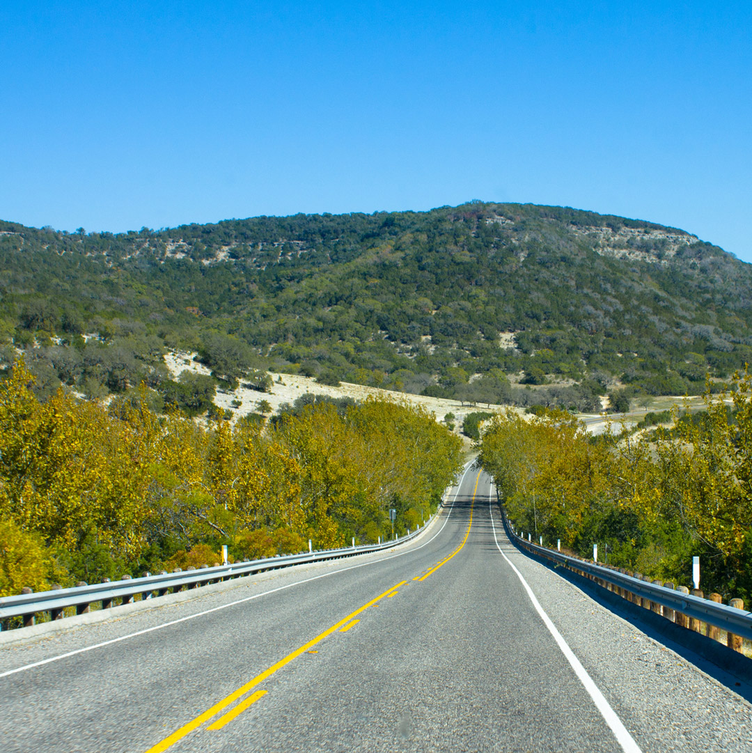 open road stretching toward scenic green hills in Texas