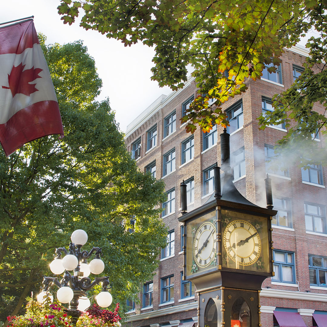 old clock spewing steam next to a Canadian flag in Vancouver