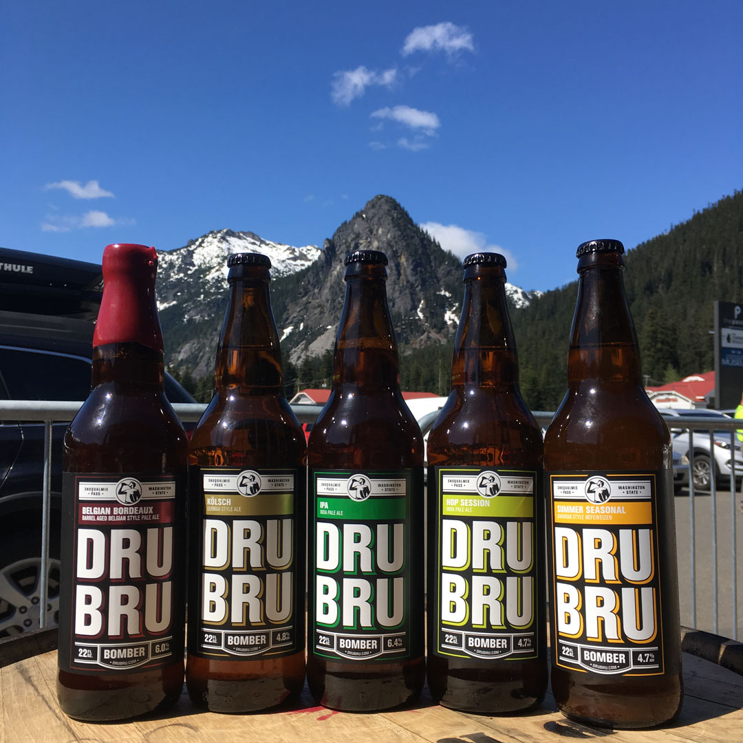 five bottles of beer sitting on a barrel with a mountain in the background
