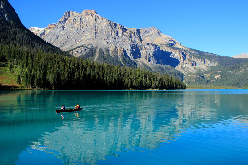 A canoe floats on the surface of Emerald Lake with the mountains reflected in the surface.