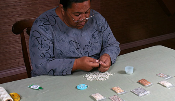 An artisan carefully crafts a necklace of niihau shells.
