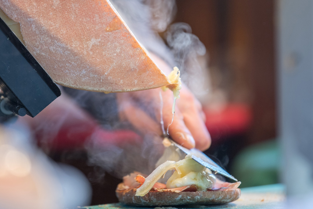 a chef scrapes cheese from a raclette wheel with a hot knife