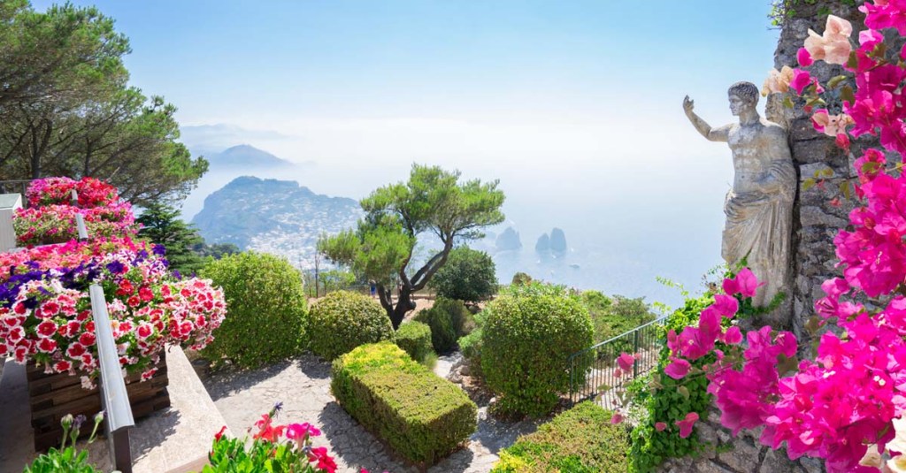Pink flowers and the statue of a man overlook the island coastline of Capri.