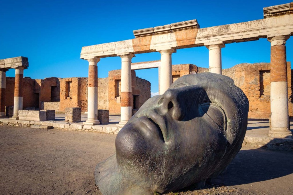 Ruins and a large bronze head in ancient Pompeii city, Italy.