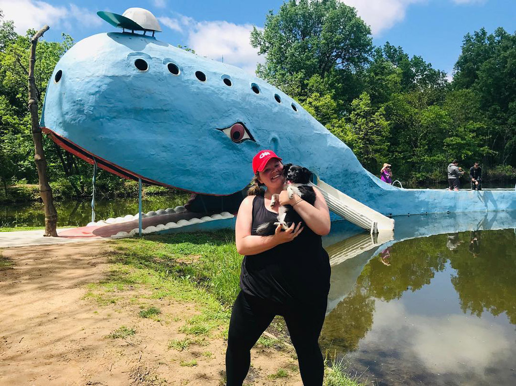 woman wearing black holding a dog in front of a constructed blue whale in Oklahoma